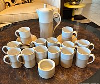 Full set arranged on table: coffee pot, 12 mugs, stacked saucers, sugar bowl