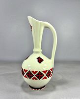 Left profile view of cream glazed ewer with red/black geometric band and diamond motifs