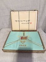 Open box showing turquoise interior panel and calligraphy on lid