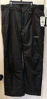 Front view of black Arctix snow pants showing tags, pockets, waist adjusters