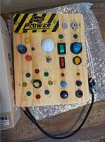 Front view of busy board showing all switches, buttons, lights and attached cord