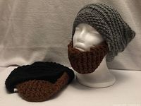 Grey beanie with brown beard displayed on mannequin; black hat with beard beside