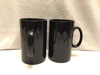 Two tall glossy black mugs side by side showing handle and height
