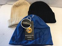 Three beanies: blue Buff with tag, cream rib knit, black rib knit