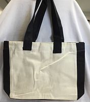 Front view of cream and black canvas tote showing body and straps