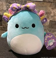 Front view of Irina axolotl plush showing face, belly, gills, and headband with attached tag