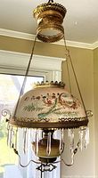 Full view of hanging oil lamp showing brass frame, painted shade, prisms, font, canopy