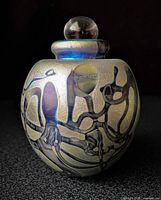 Front view of iridescent round perfume bottle with stopper showing abstract metallic design
