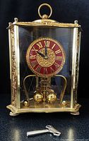 Front view of brass and glass 400-day clock with red dial and key