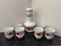 Full decanter and six cups showing floral pattern