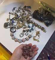 Overview of assorted vintage costume jewelry spread on table and hand holding loose beads