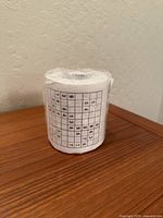 Front view of sealed Sudoku toilet paper roll on wooden surface