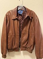 Front view of brown leather bomber jacket on hanger