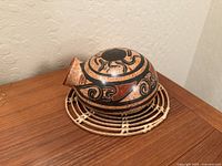 Side view of pottery on woven stand showing decoration and spout