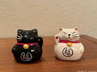 Front view of black and white maneki-neko shakers on wood surface