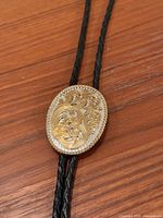 Front view of gold-tone floral oval slide on black braided cord