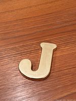 Full view of brass letter J paperweight on wooden surface