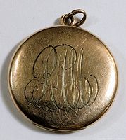 Front of round locket showing engraved monogram and bail