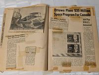 Open scrapbook showing articles on $25 million Canadian space program and hovercraft vehicle plus mounted stamp clippings