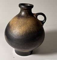 Front view of bulbous black and gold vase with handle