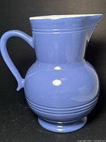 Full side view of blue Emile Henry jug with handle and pedestal base.