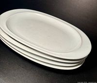 Stack of four white oval plates, side angle