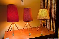three teak tripod table lamps lit on wooden surface