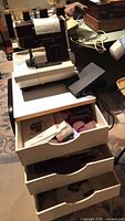 Serger on top of drawer unit with foot pedal, thread cones, drawers open showing contents