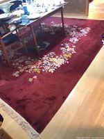 Full view of burgundy rug under table showing floral border and fringe edge