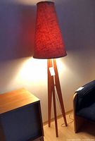 Full view of illuminated teak tripod floor lamp with tapered red woven shade