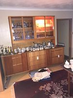 Full view of two-piece teak sideboard with glass hutch populated with dinnerware