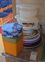 Stack of chargers, paper plates, food containers and decorative tins on countertop