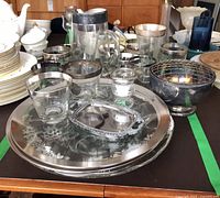 Group view of silver-rimmed glassware, platters, trays, candle holder and flower frog