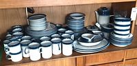 Full dinnerware set on shelf showing variety of plates, mugs, cups, teapot, creamer, sugar
