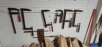Seven clamps hanging on pegboard, six metal F-style and one wooden hand screw clamp