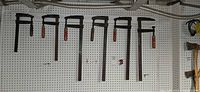 Seven F-clamps hanging on pegboard showing overall quantity and varying bar lengths