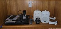 Shelf showing DVD player, cordless phone, stack of DVDs, remotes, pair of speakers