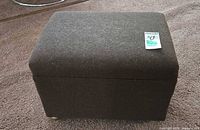 Overall view of dark brown upholstered footstool on casters