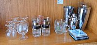 Overview of all barware on shelf: snifters, tumblers, mug, shakers, coasters