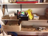 Shelving with various hardware items including boxes, paint tray, bag of plumbing parts, grey raceway and coiled cable