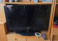 Front view of Samsung LN32A300J1D TV on stand with remote and cable