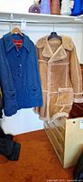 Blue wool cape and tan shearling coat hanging on rack