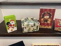 Three boxes: green Santa, pine branch, red snowman book