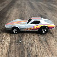 Side view of metallic silver Corvette Stingray with orange/magenta stripes and Stingray tampo