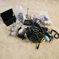 Pile of assorted cables, black clamshell device, silver spherical devices, zip bags with accessories on carpet