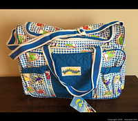 Front view of Teletubbies diaper bag showing pattern, logo pocket, attached tag and shoulder strap