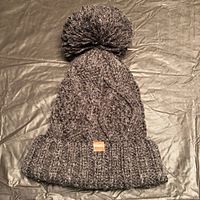 Full view of dark grey cable-knit beanie with pom-pom and Roots tag
