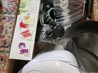 Boxed kitchen items showing mandoline box, EVOO bottle, soap dispenser, lids and skillet