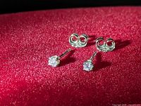 Pair of 14K white gold diamond stud earrings with butterfly backs displayed on red fabric