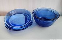 Two Pyrex pie plates stacked beside three Anchor Hocking bowls, full lot overview